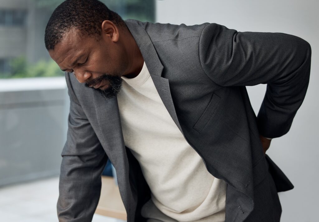 A man wearing a gray blazer hunches over and presses his back before neck and spine therapy in Charleston.