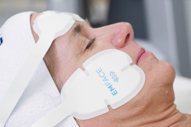 A woman is lying down with Emface applicators on her face for body contouring in Mt. Pleasant, SC.