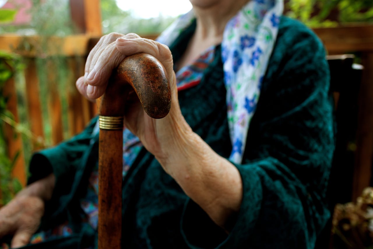 A woman uses a cane, struggling with mobility and frailty as she ages. Many such patients can benefit from early intervention with strength training for longevity in Charleston.